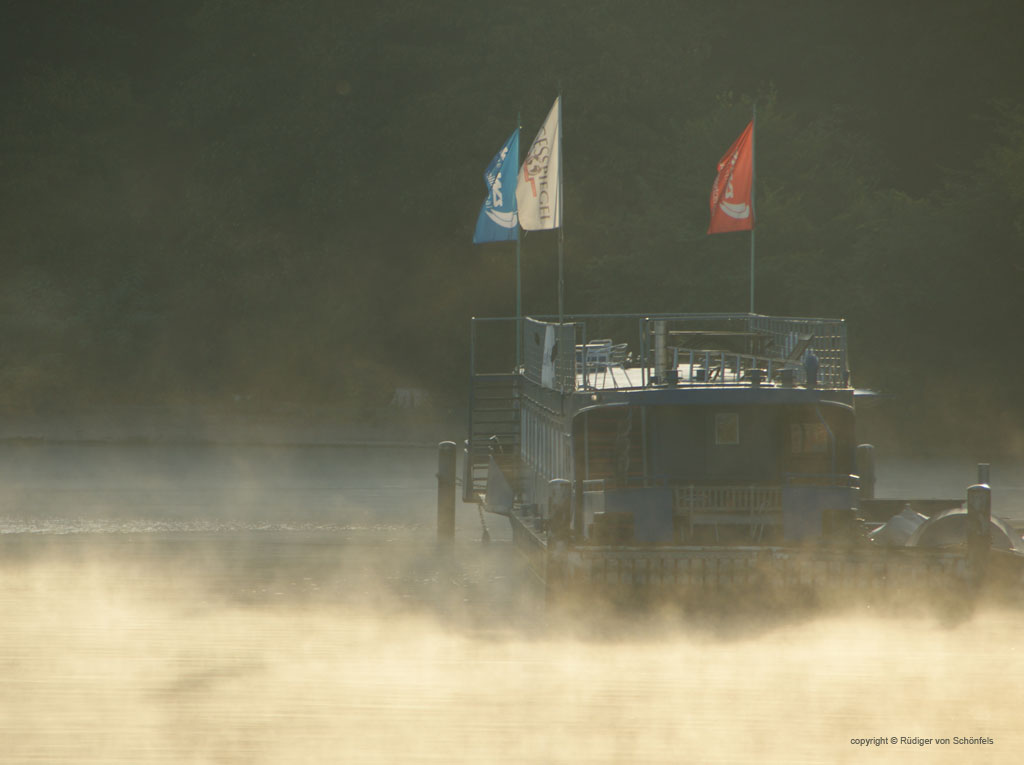 Hausboot mit wehenden Fahnen bei "dampfendem" Nebel in der Morgensonne